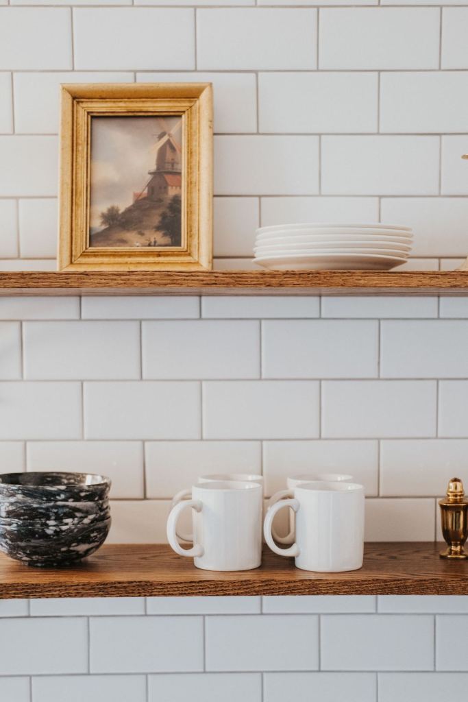 Open shelf with a gilt-framed painting, mugs and stoneware