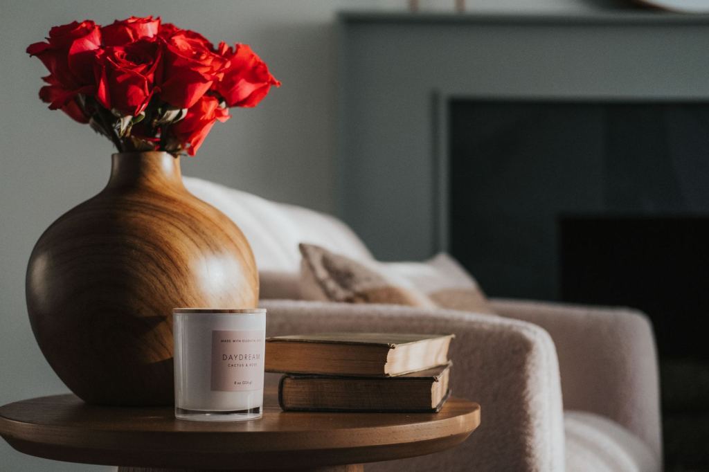 Wooden vase of red roses beside a candle and old books