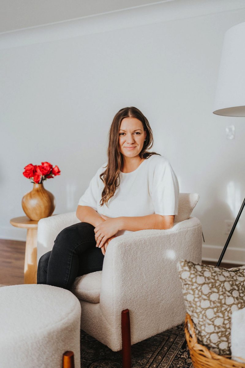 Gabi Gatea seated in a cream boucle armchair beside a vase of red roses
