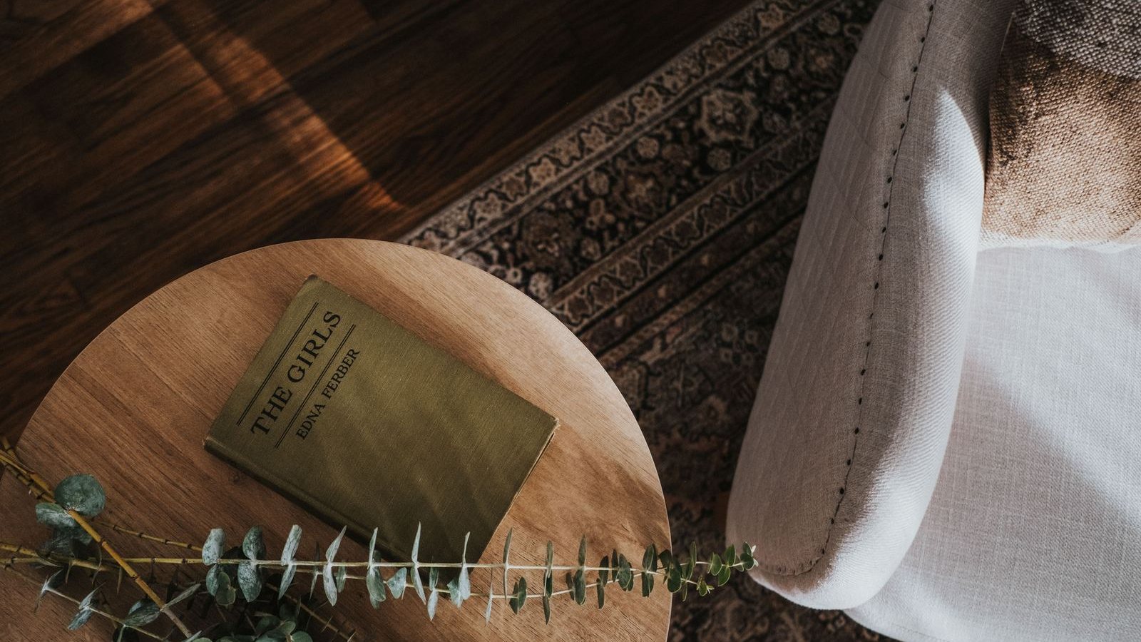 Olive cloth-bound book on a round oak side table beside a linen armchair and vintage rug
