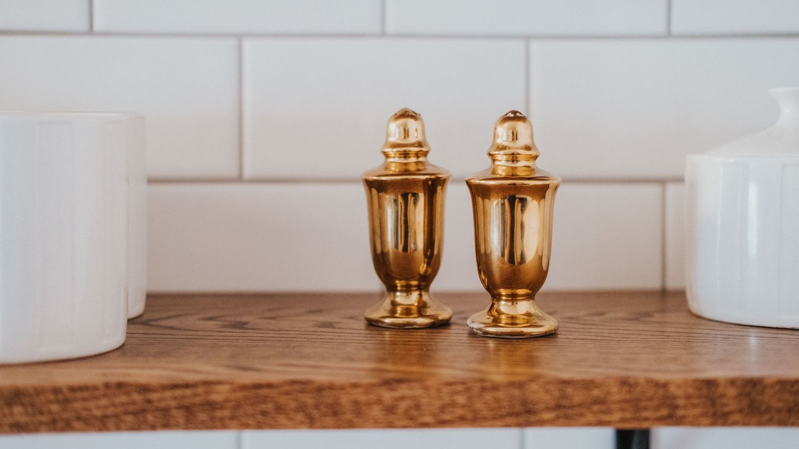 Brass salt and pepper shakers on a walnut shelf against white subway tile