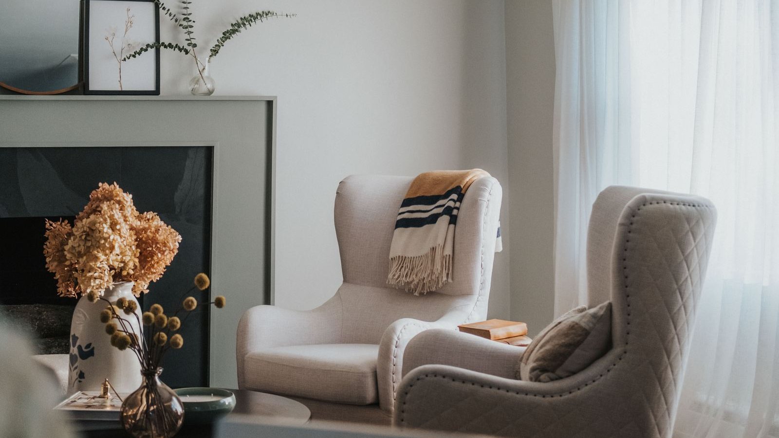 Sunlit living room with dried hydrangeas, two cream wingback chairs and sheer curtains